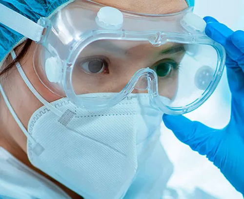 Chica vestida con equipo de protección individual compuesto por gafas transparentes, mascarilla, gorro y guantes de color azul